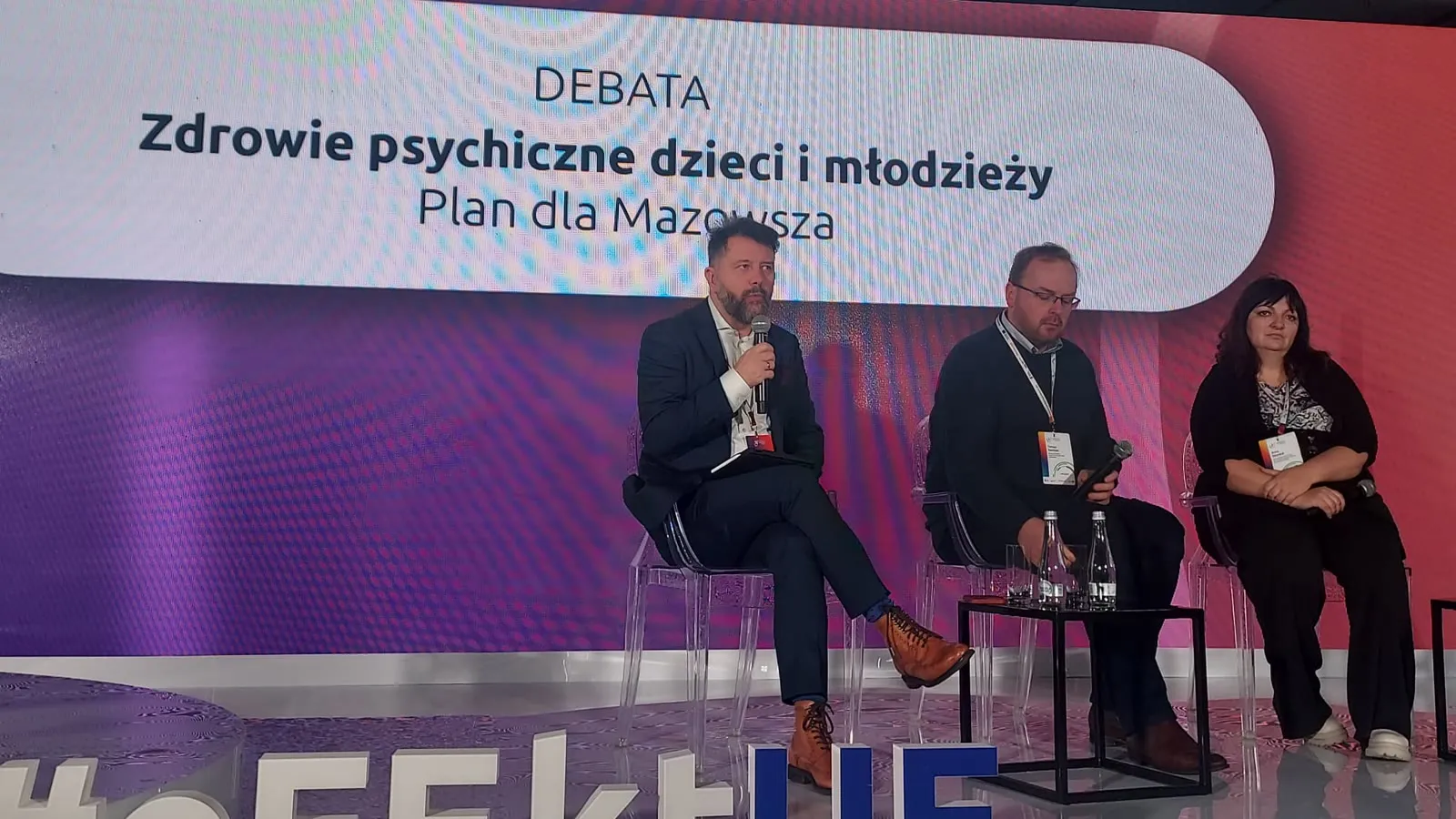Rafał Szymański prowadzi debatę, obok Tomasz Rowiński i Anna Depukat, na ekranie tytuł debaty