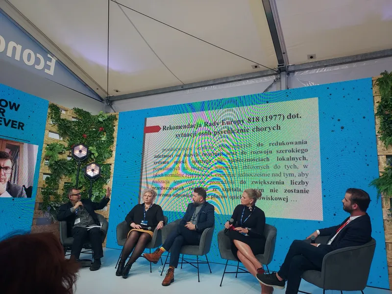 Krzysztof Olkowicz pointing at a slide with Council of Europe Recommendation 818 from 1977 on the situation of the mentally ill, with the other debate participants sitting next to him