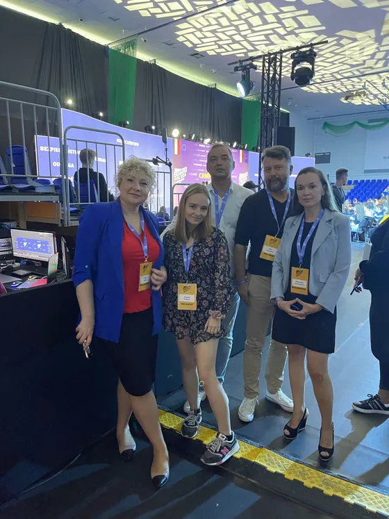 Five participants of the child psychiatry debate standing with badges next to the stage at Campus Polska Przyszłości, with the stands and the audience behind them