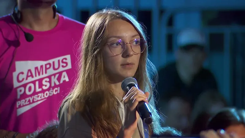 A young woman in glasses asking a question into a microphone from the audience, next to a volunteer in a pink Campus Polska Przyszłości T-shirt